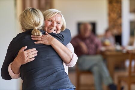 Daughter visits happy mother in nursing home and hugs her in greetingの写真素材