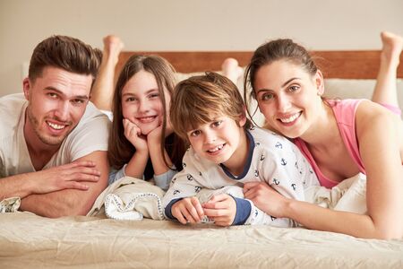Happy parents with two kids in pajamas in the morning on the bed