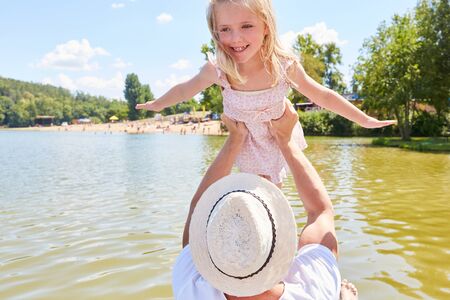 Father lifts daughter up on a boat trip on the lake in the summer in amusement parkの写真素材