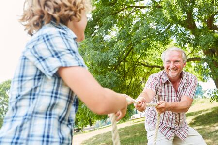 Grandfather tug-of-war with his grandson in the park or in the garden in summerの写真素材