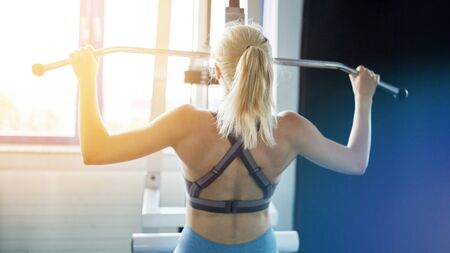 Back of a woman in back training on Latzug in the fitness centerの写真素材