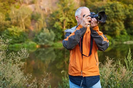Senior countryside photographer with camera in nature while photographing