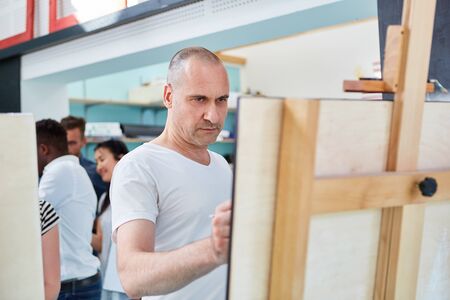 Artist paints concentrated on canvas at the easel in the art course of the community collegeの写真素材