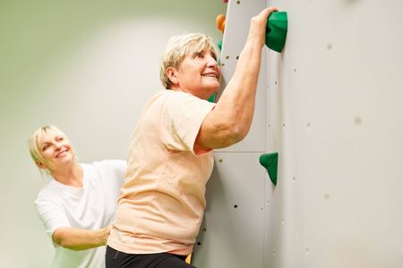 Physiotherapist gives senior woman assistance in climbing on a climbing wall