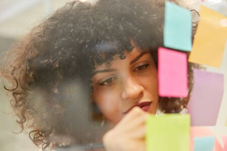 Young African businesswoman is writing down ideas on colorful notes while brainstormingの写真素材