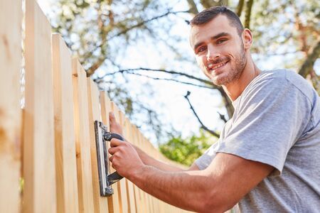 Young craftsman apprentice or handyman at fence grinding in summer in the gardenの写真素材