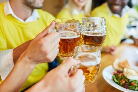 Hands hold beer glass while toasting in a bar or restaurantの写真素材