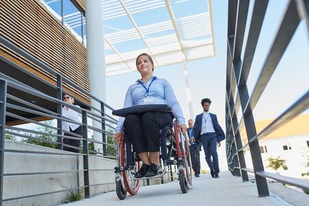 Business woman in a wheelchair in front of the office on a ramp with other workers