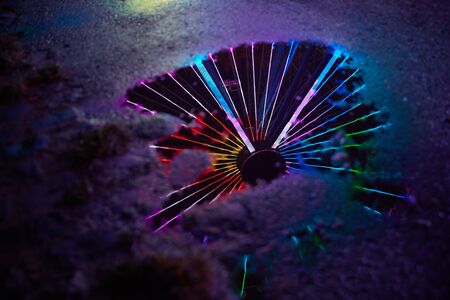 Colorful neon lights from a ferris wheel as a reflection in the water of a puddle at a folk festival at nightの写真素材