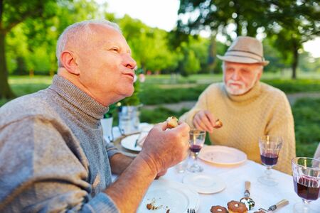 Old man enjoys eating cake in the garden with friendsの写真素材