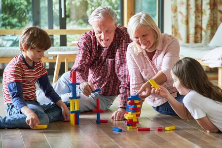 Grandparents are stacking building blocks together with their grandchildren at homeの写真素材