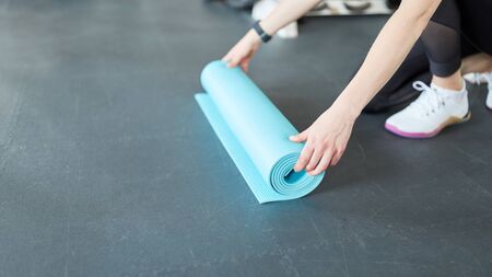 Young woman rolls out a yoga mat in the fitness center before workoutの写真素材