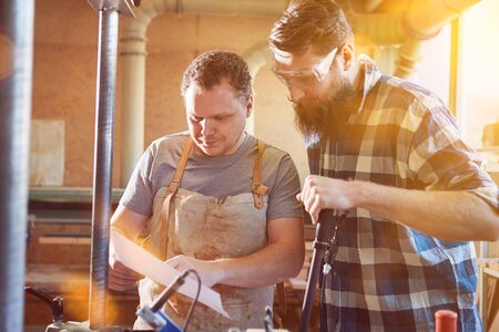 Two carpenters process furniture orders in their workshop