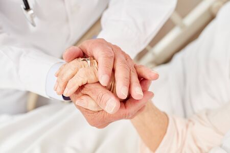 Doctor consoles a sick elderly woman and holds her hand caring in his hands