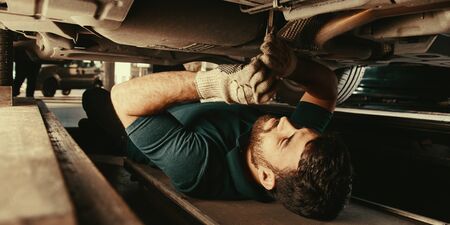 Mechanic lies under a car during repair in the car workshopの写真素材