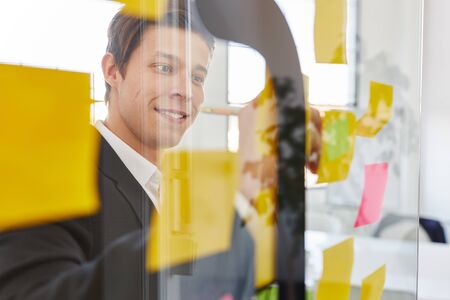 Start-up businessman takes notes on paper on glass wall