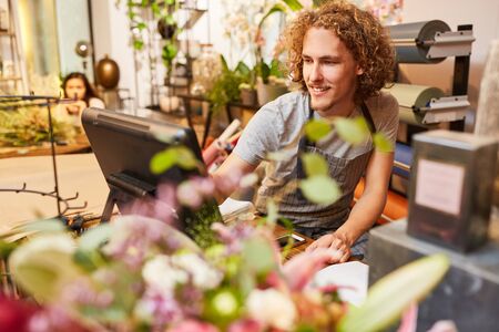 Young man as a cashier or seller at the cash register in the flower shopの写真素材
