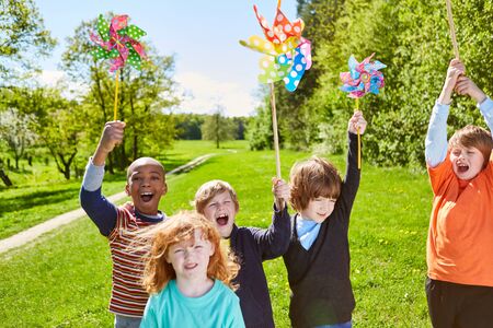 Group of kids with pinwheel happily celebrates a kid's birthday in the summer in the park