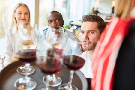 Waitress serves guests on a tray glasses with red wine in the restaurantの写真素材