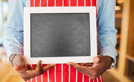 Hands of a service worker hold empty chalk board in the restaurant for marketingの写真素材