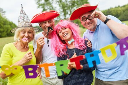 Four seniors in colorful costumes celebrate a birthday party in the gardenの写真素材