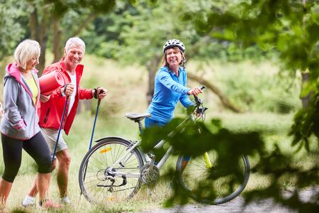 Seniors exercise fitness in nature with mountain bikes and hiking polesの写真素材