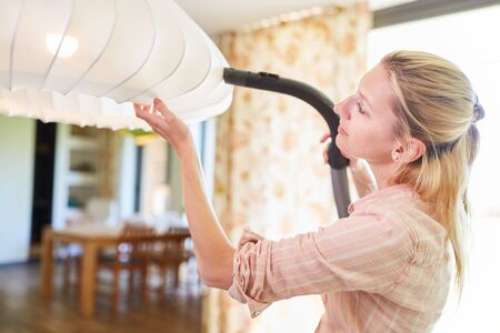 Maid or cleaner at vacuuming a lamp at home