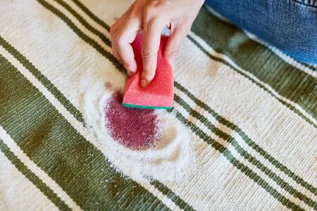 Hand with sponge while removing red wine stains with salt on carpet