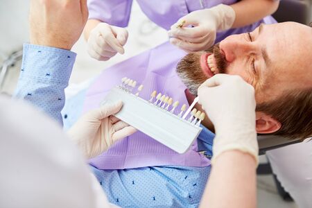 Man as a patient adjusting the tooth color in the professional teeth whitening