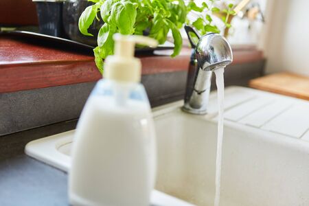 Liquid soap next to faucet with running water in the kitchenの写真素材