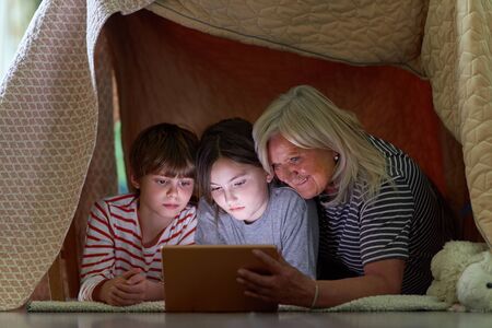 Kids and grandma using tablet computer while surfing the internet under blanket as a tentの写真素材