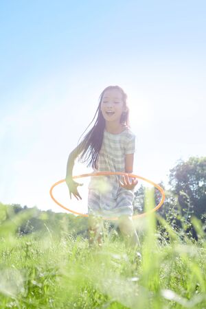 Happy girl is playing with a hoop on a meadow in natureの写真素材