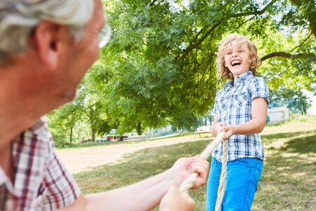 Laughing boy in tug of war competition in the park in summer with the grandfather