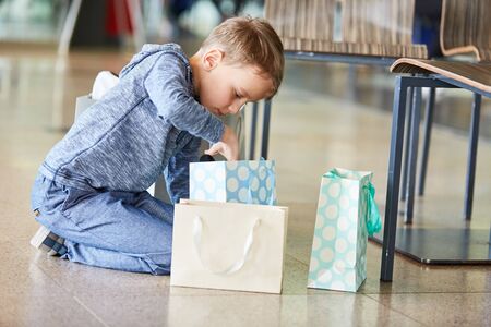 Boy unpacks his presents curiously in the shopping bags in the mallの写真素材