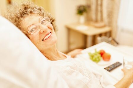 Happy senior woman is lying in bed in her senior citizen home or retirement homeの写真素材