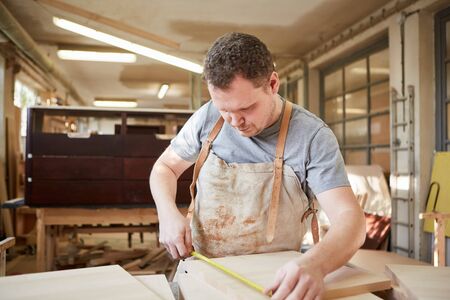 Carpenter apprentice as a furniture maker when measuring wood with a measuring tape