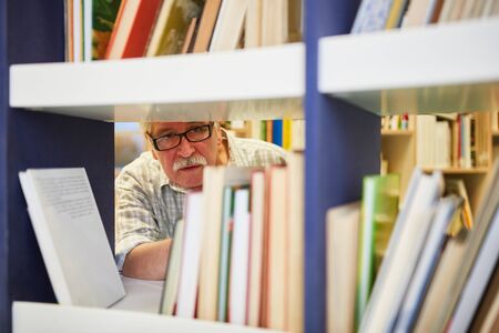 Senior as a scientist researching in a library with many booksの写真素材