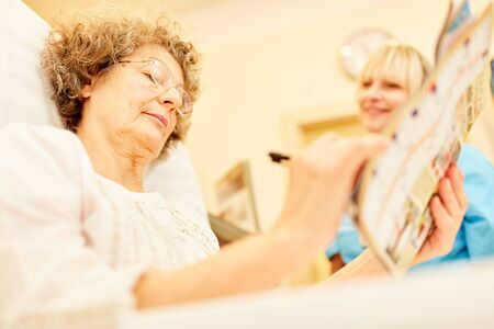 Senior woman as a patient with dementia solves crossword puzzle in nursing homeの写真素材