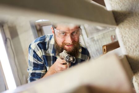 Painter using the spray gun while painting furniture with wood glaze in carpentry