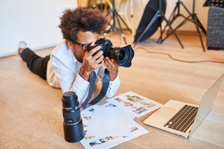 Young photographer in front of the laptop with camera and selection of print photosの写真素材