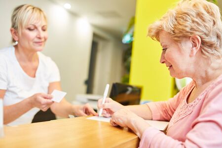 Elderly patient and receptionist at registration at the reception at the doctorの写真素材