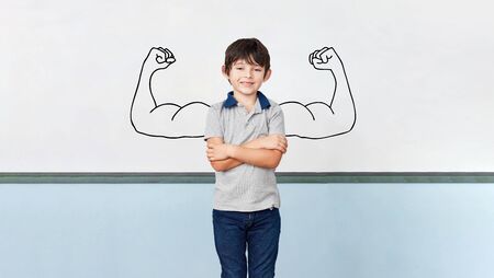 Child as a student with arms crossed in front of muscles on blackboard in school