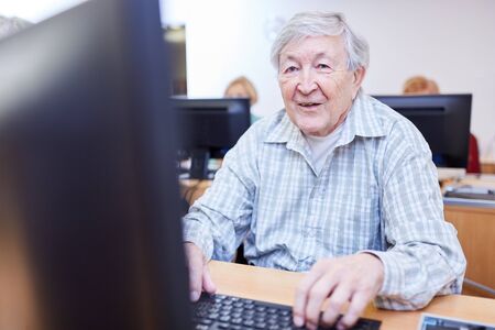 Pensioners in a retirement home sit on a PC in a computer course and learn how to use the Internetの写真素材