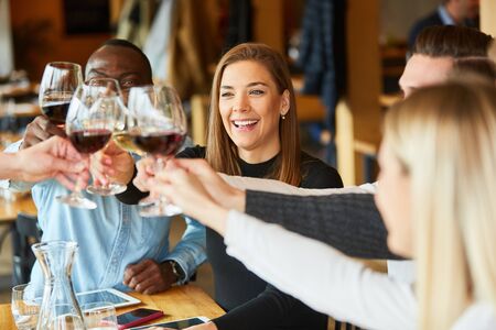 Group of young people celebrates birthday in the restaurant and toast with glass of wine