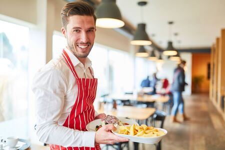 Man as a friendly waiter in training serves food in the restaurant