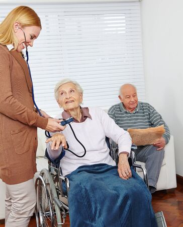 Woman from nursing service measures blood pressure in elderly woman in a wheelchair at homeの写真素材