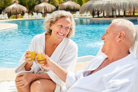 Happy couple seniors relaxing with orange juice at the spa pool by the hotelの写真素材