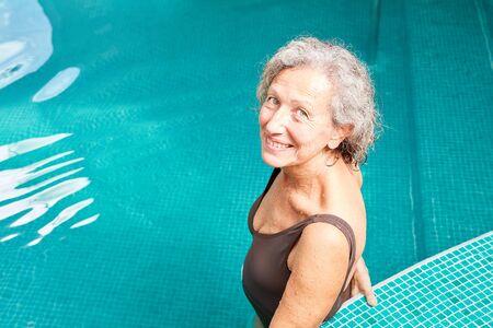 Vital senior woman stands smiling in the swimming pool and exercises her fitness