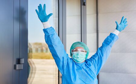 Doctor in protective clothing cheers in front of clinic after success in fighting coronavirus and...
