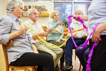 Seniors with dementia do an exercise with colorful ribbons for interactionの写真素材